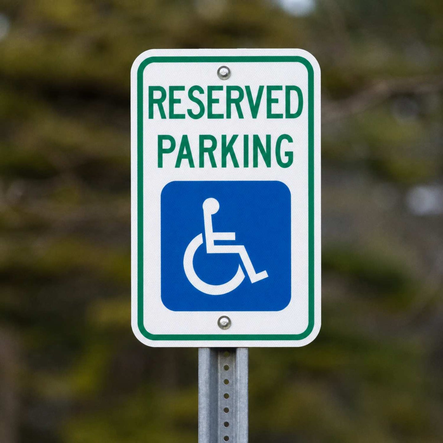 White 12x18 ADA Reserved Parking sign with green text and blue handicap symbol on a metal post.