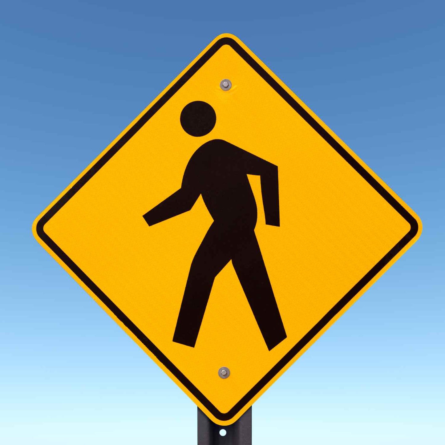 Yellow diamond-shaped W11-2 pedestrian crossing sign with a black symbol on an aluminum post.