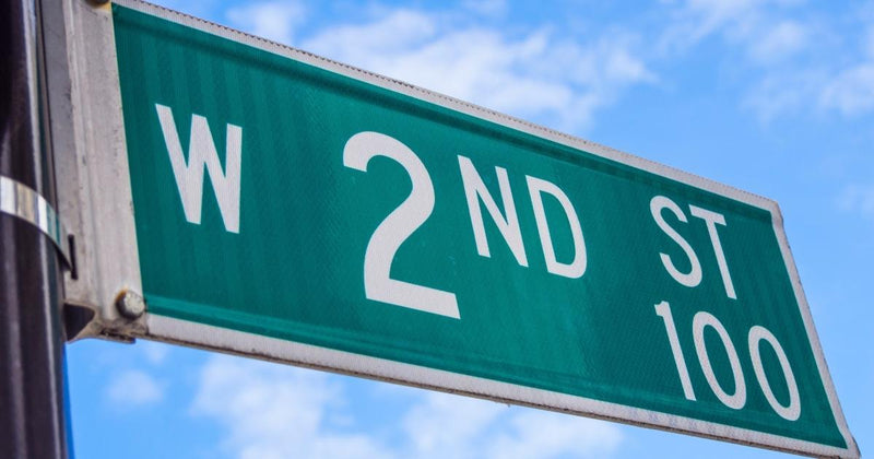 Green W 2nd St street sign with white lettering against a bright blue sky with light clouds.
