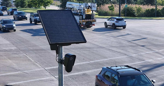 A Flock AI camera and panel mounted on a metal pole in a parking lot.