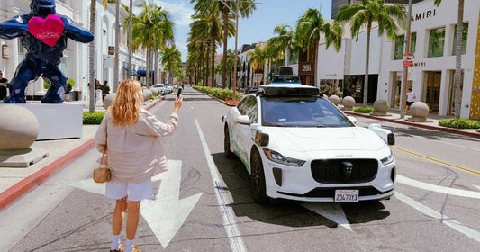 A woman taking a picture of a Waymo car in the middle of the street in California