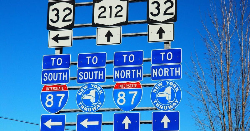 Blue highway signs for Interstate 87 and New York Thruway against a clear sky.