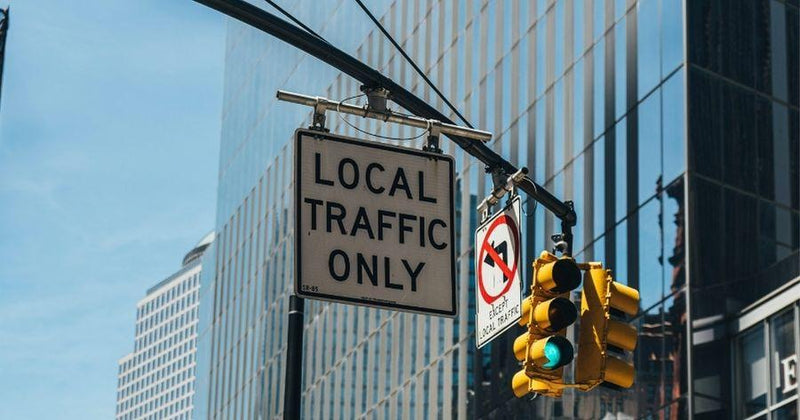 Local traffic only sign and a green traffic light hanging against a modern glass skyscraper in a city.