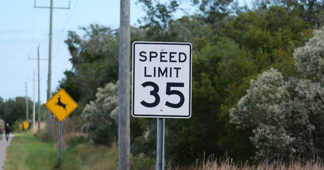 White rectangular speed limit 35 sign next to a yellow deer crossing warning sign on a rural roadside.