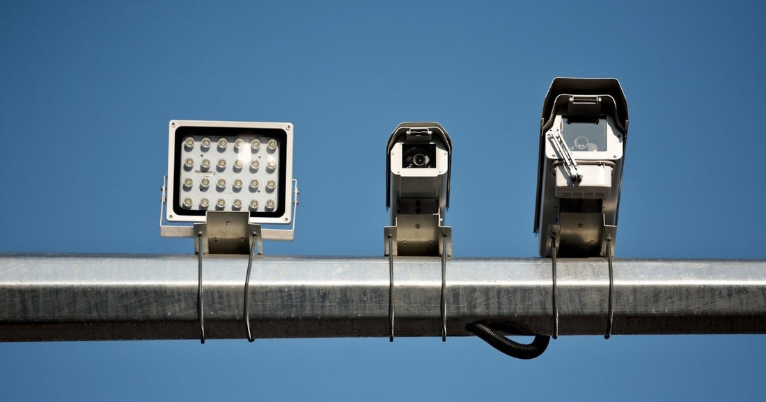 Three traffic surveillance cameras mounted on a metal pole against a clear blue sky.