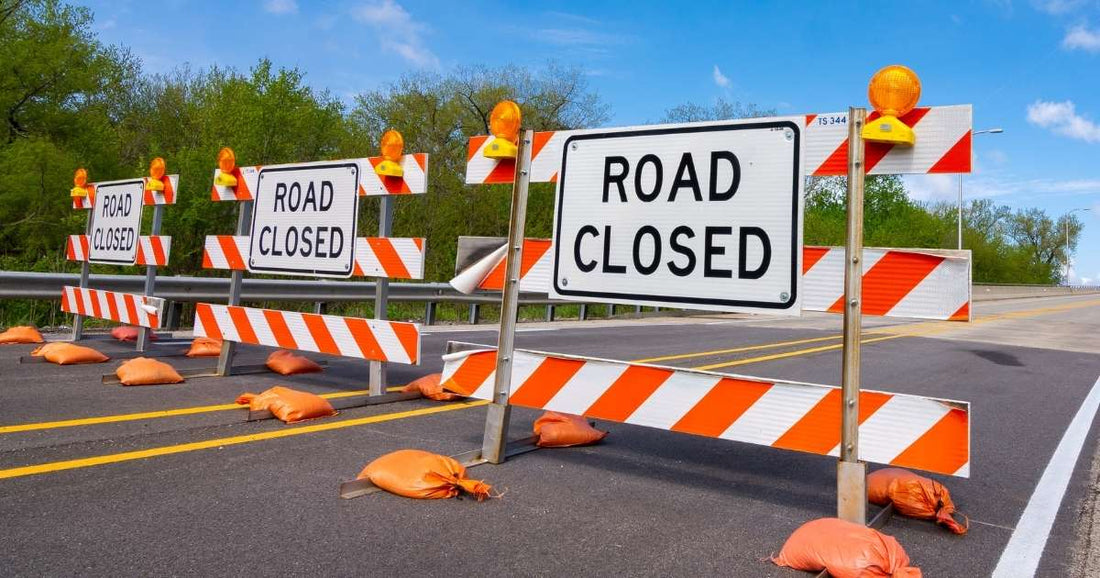 Road closed signs with orange and white striped barricades and flashing amber lights on a highway.