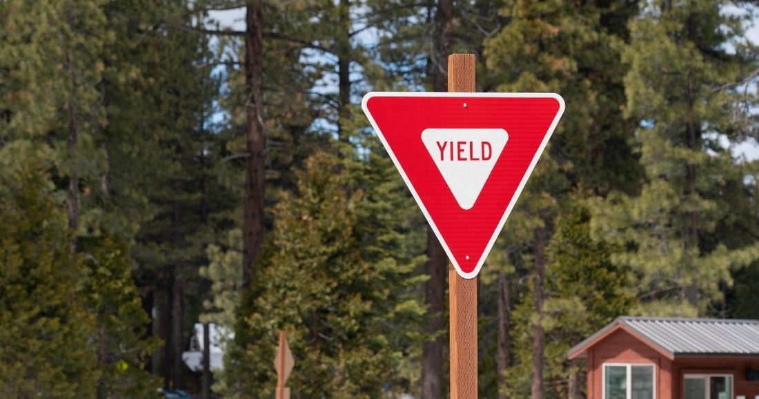 Red and white triangular yield sign mounted on a wooden post against a forest background.