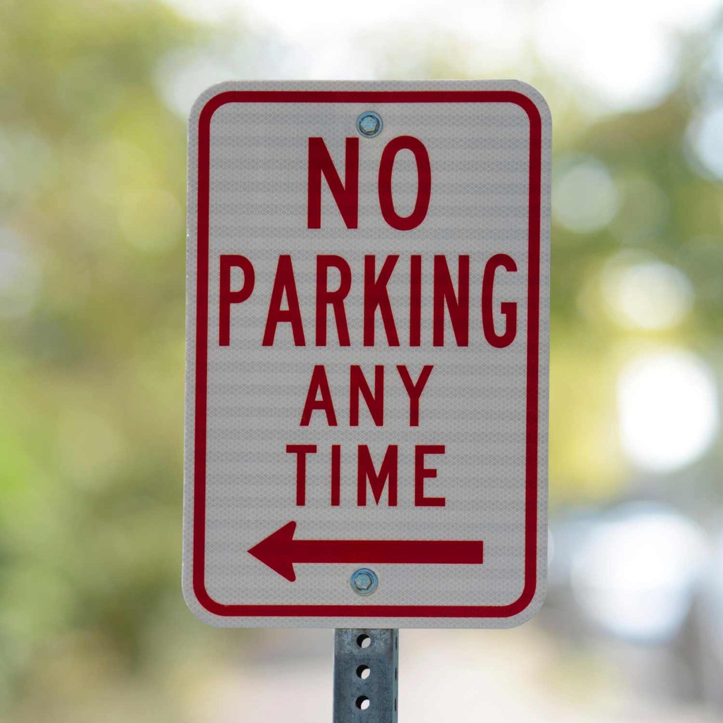 White 12x18 "NO PARKING ANY TIME" sign with red text, universal symbol, and left arrow on a metal post.