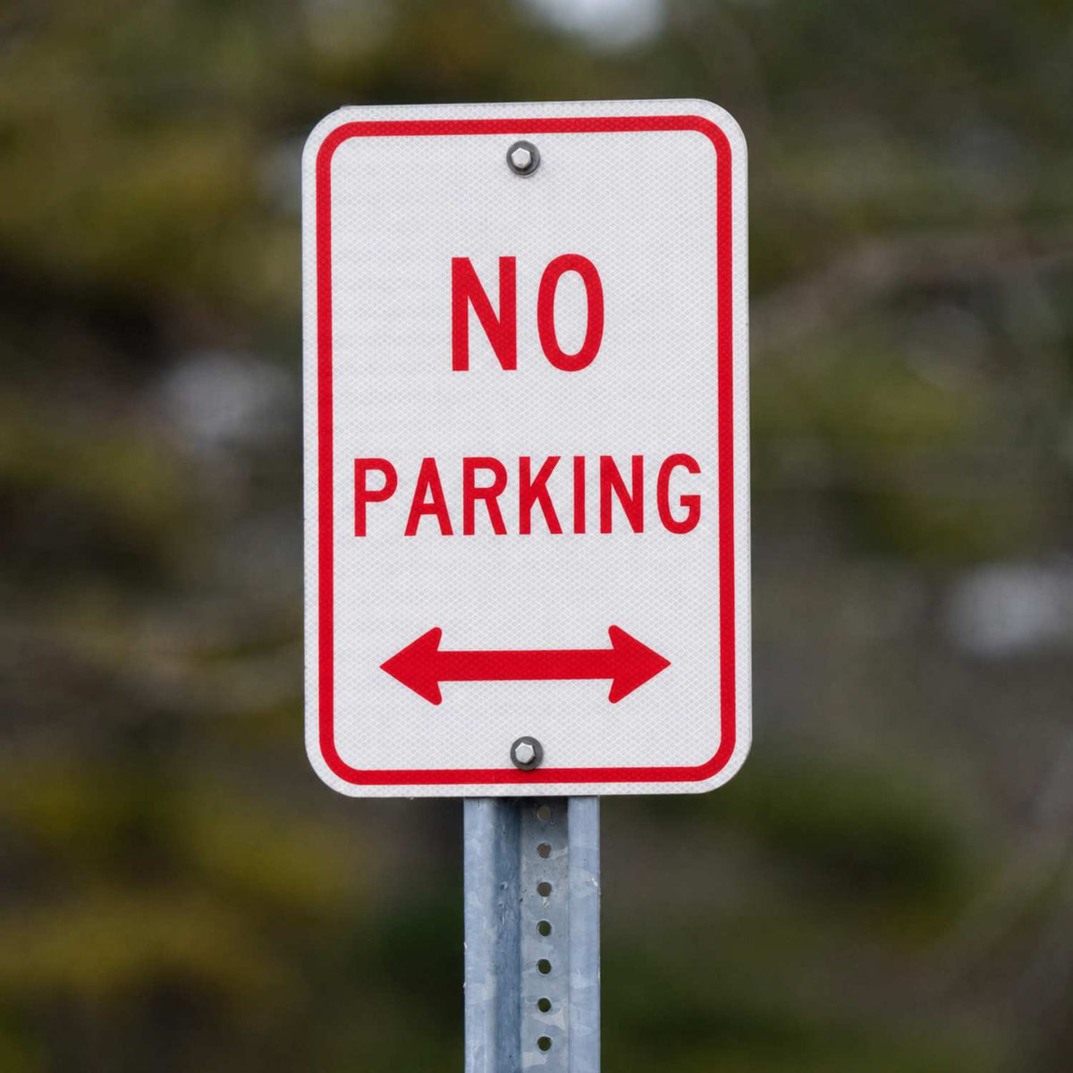 White 12x18 "NO PARKING" sign with red text and double arrows, mounted on a metal post.