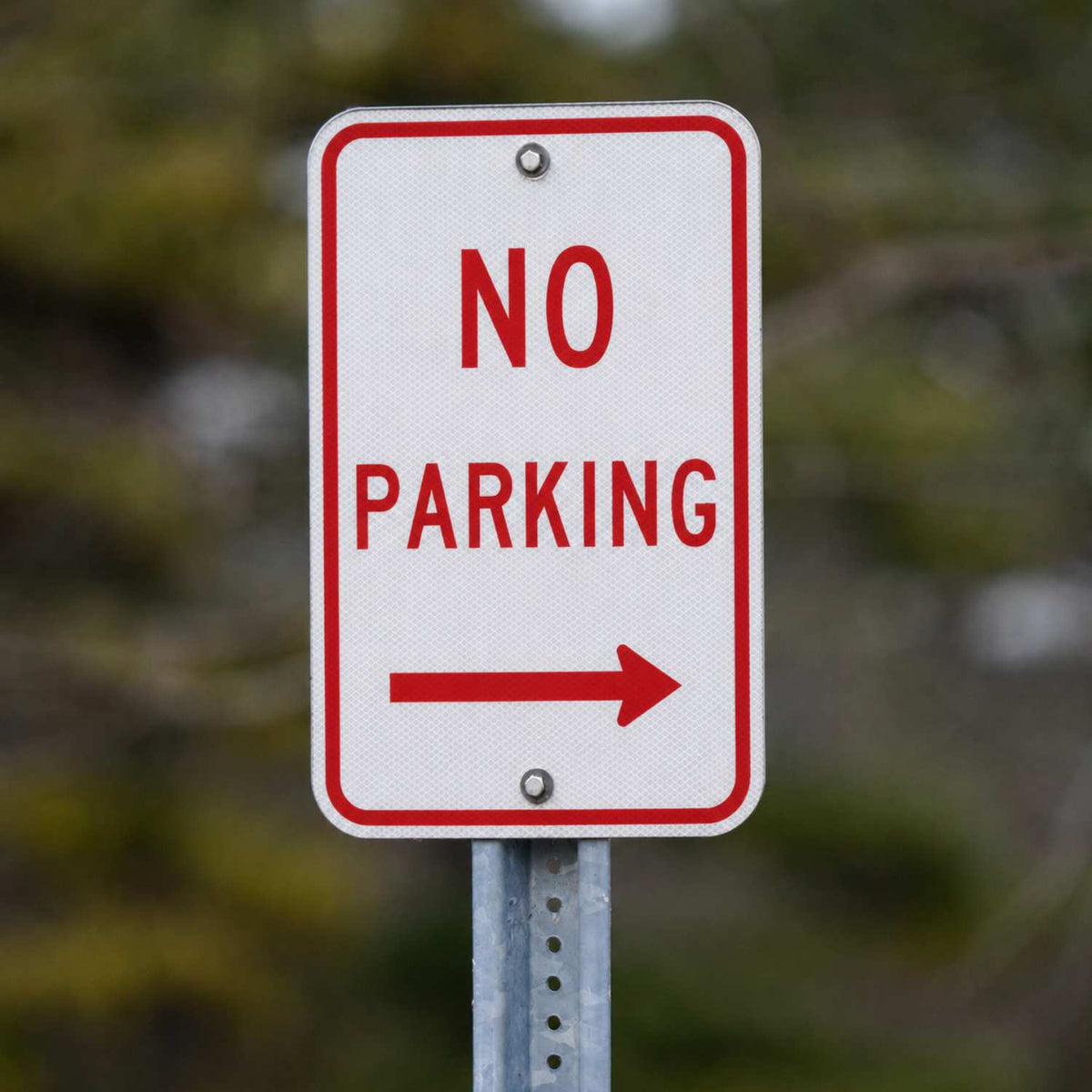 White 12x18 "NO PARKING" sign with red text and a right arrow, mounted on a metal post.