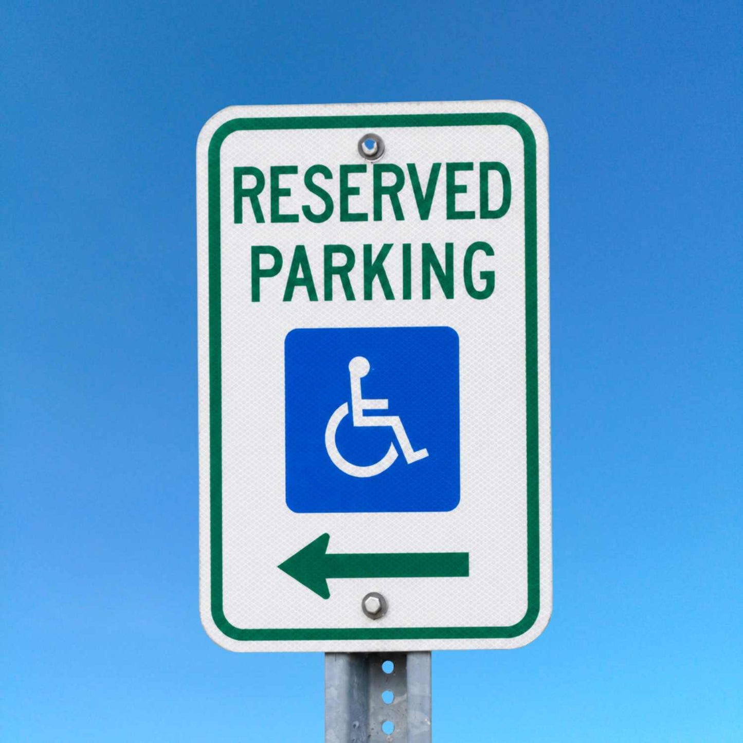 White 12"x18" Reserved Parking sign with green text, blue handicap symbol, and left arrow.