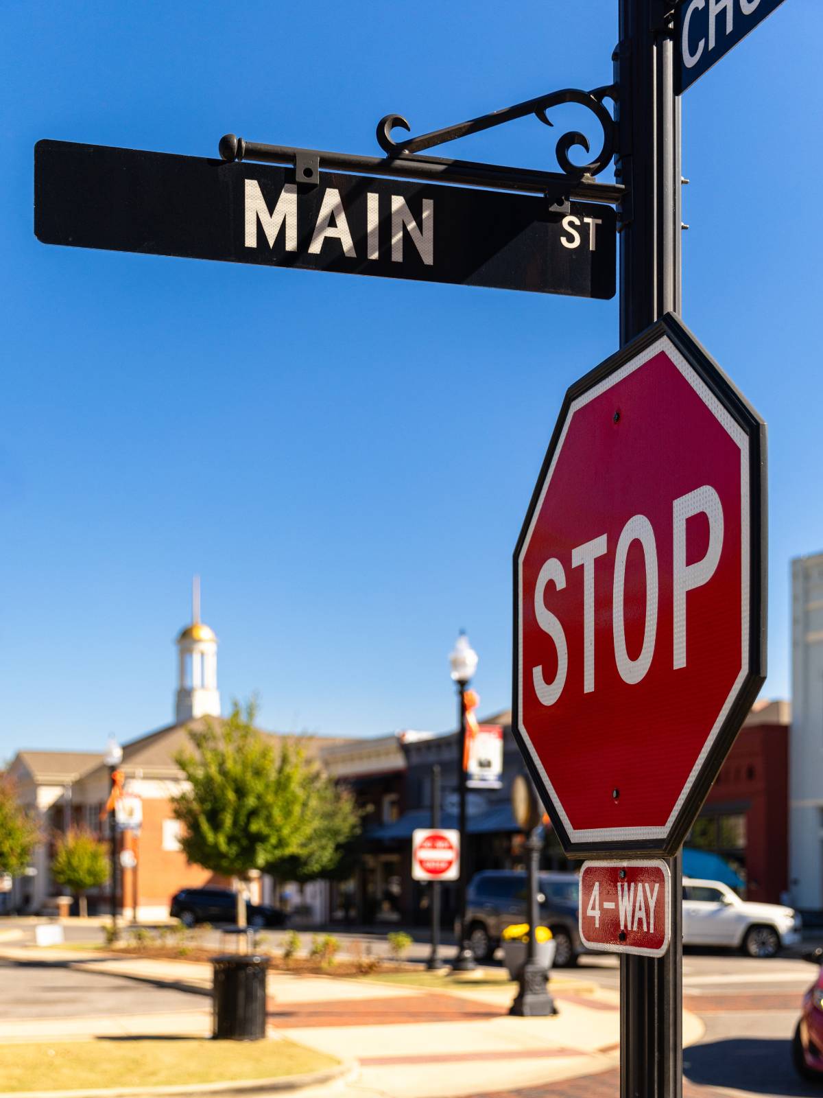 Main street name sign on top of stop sign and 4 way sign in neighborhood background